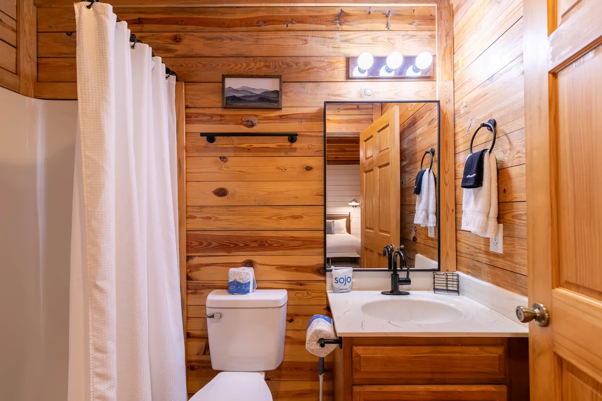 A rustic bathroom with wooden walls, a functional mirror and sink area, and a shower with a curtain. The inviting mood suggests a calm, refreshing space to unwind after outdoor adventures.